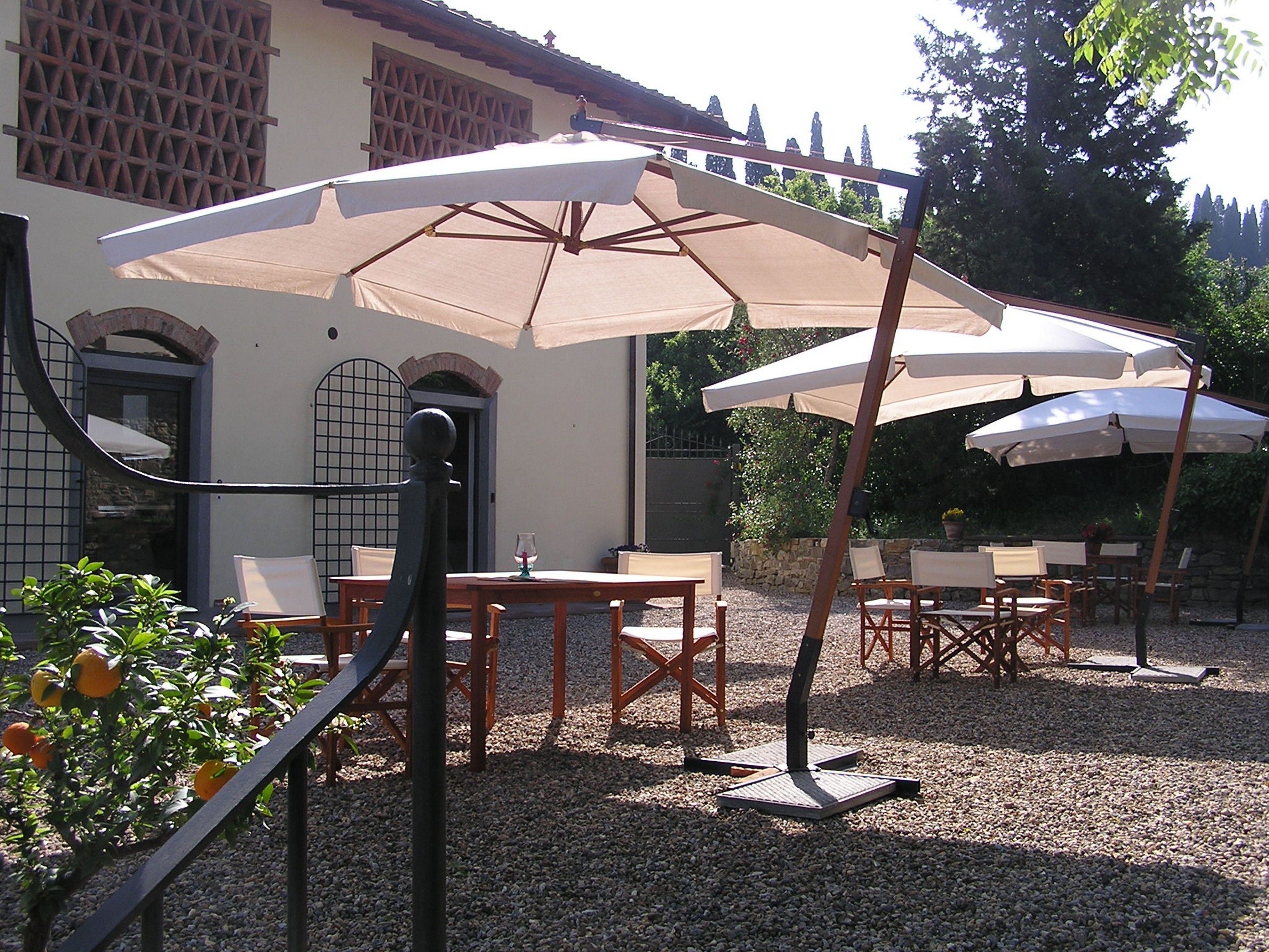 Un patio al aire libre con mesas y sillas, sombrillas grandes y un edificio al fondo.