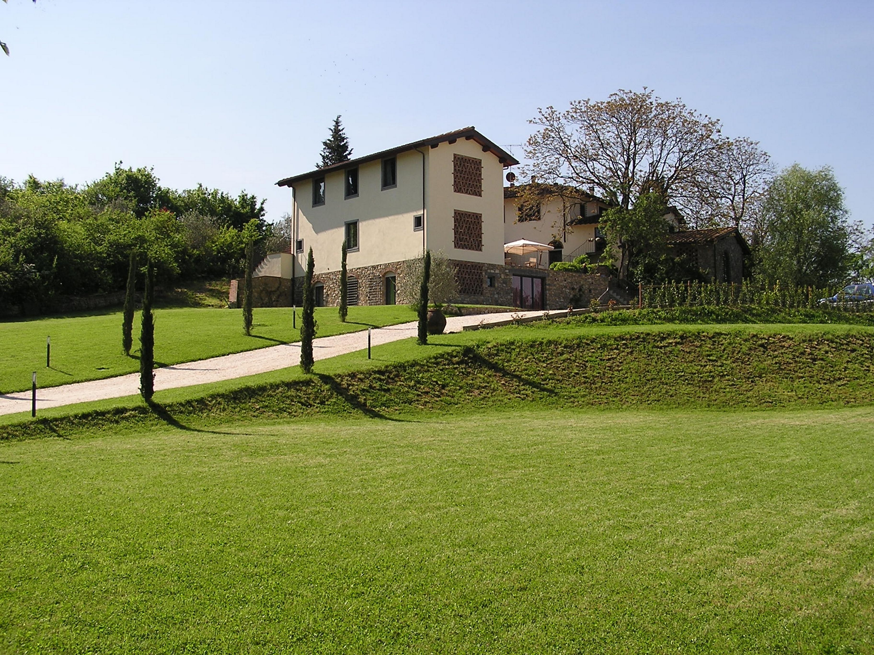 Un bâtiment à deux étages, doté d’une façade en pierre et d’un toit plat, entouré d’une pelouse bien entretenue et de quelques arbres.