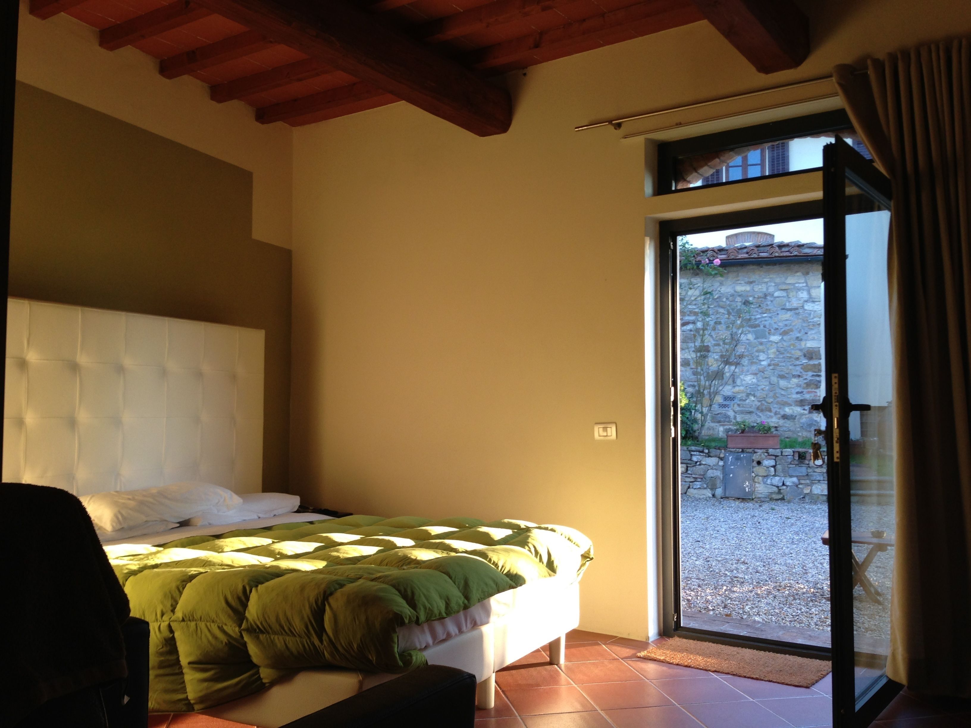 Ein Schlafzimmer mit Bett, Holzboden, einer Tür zu einem Außenbereich und einer dahinter sichtbaren Steinwand.