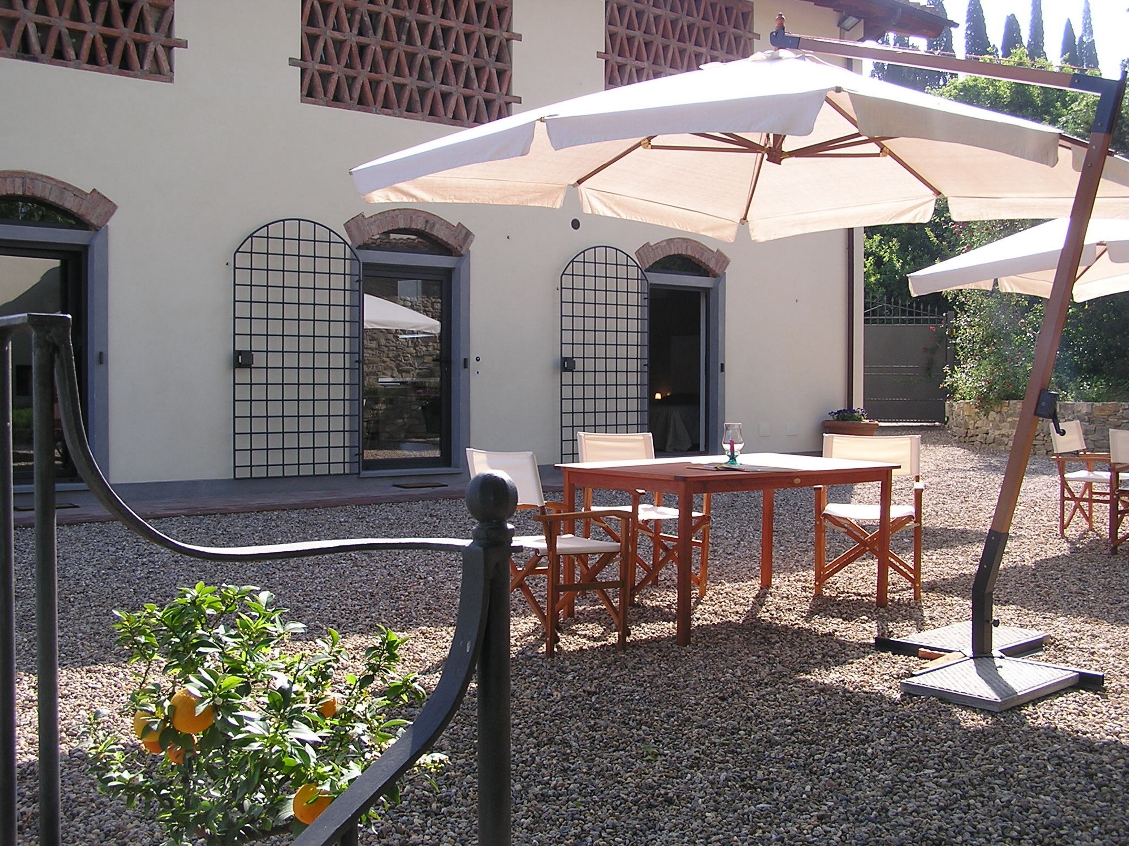 Un área de estar al aire libre con mesas y sillas, una pérgola con dosel blanco y suelo de grava.