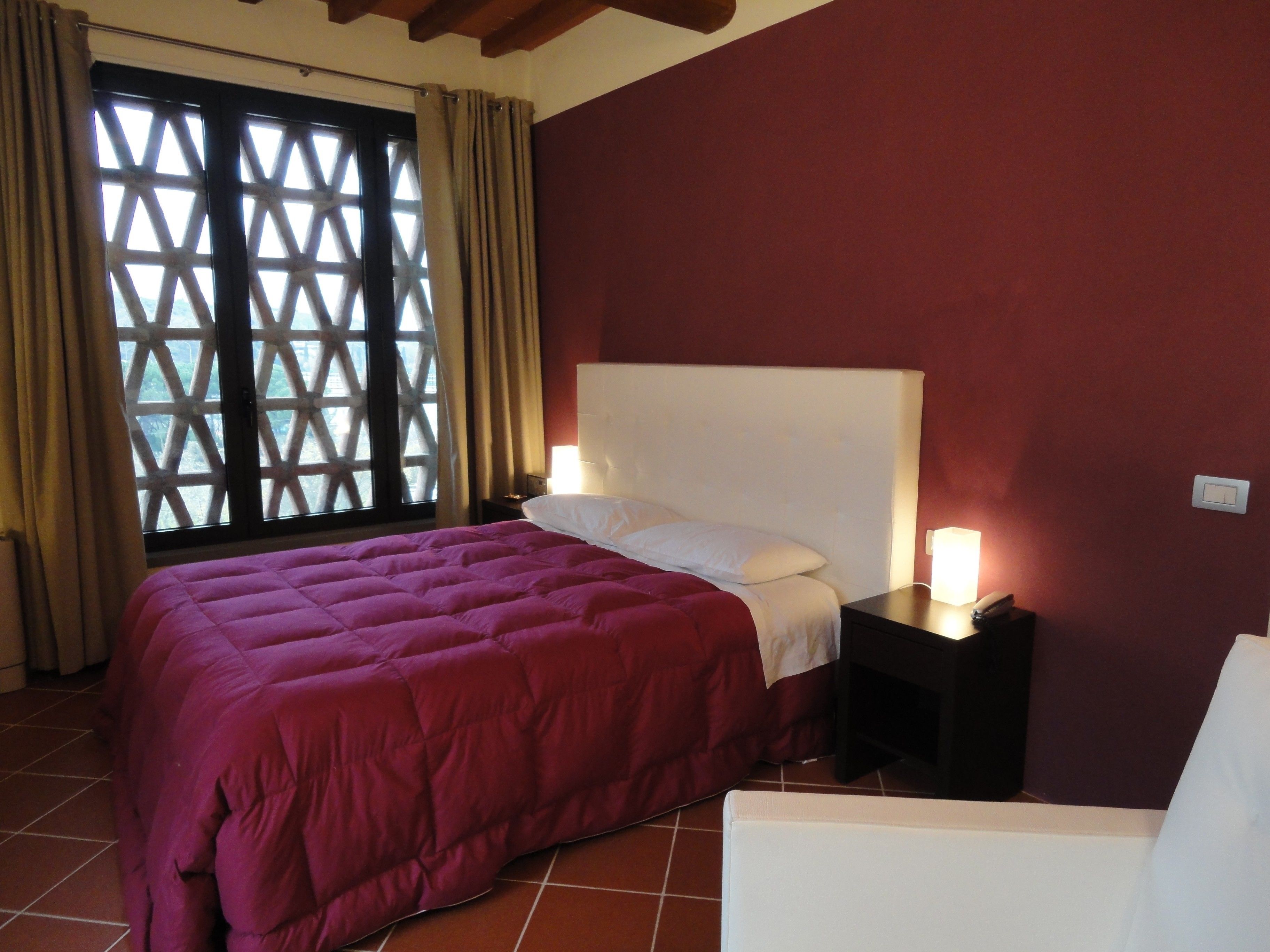 A bedroom with a large bed, a nightstand with a lamp, and a window with a lattice design.