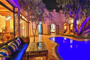 A poolside area with stone walls, a wooden bench, and a table. - Riad Dar Etto (Essaouira)
