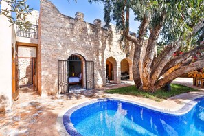 A stone building with a swimming pool, arched doorways, and a tree in the courtyard. - Riad Dar Etto (Essaouira)