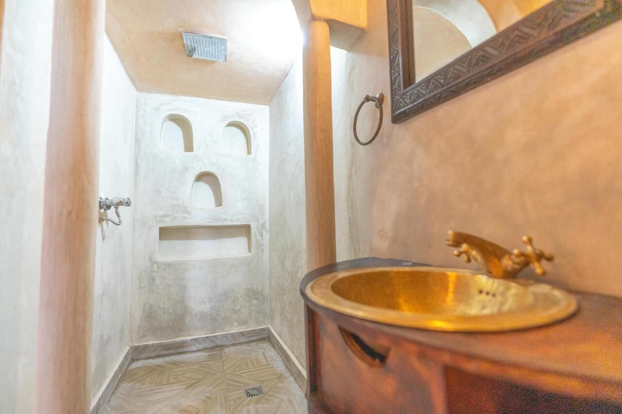 Baño con lavamanos de cobre, espejo y zona de ducha.