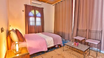 Una camera da letto con un letto, un comodino, una lampada, una sedia e un tavolino con una scatola.