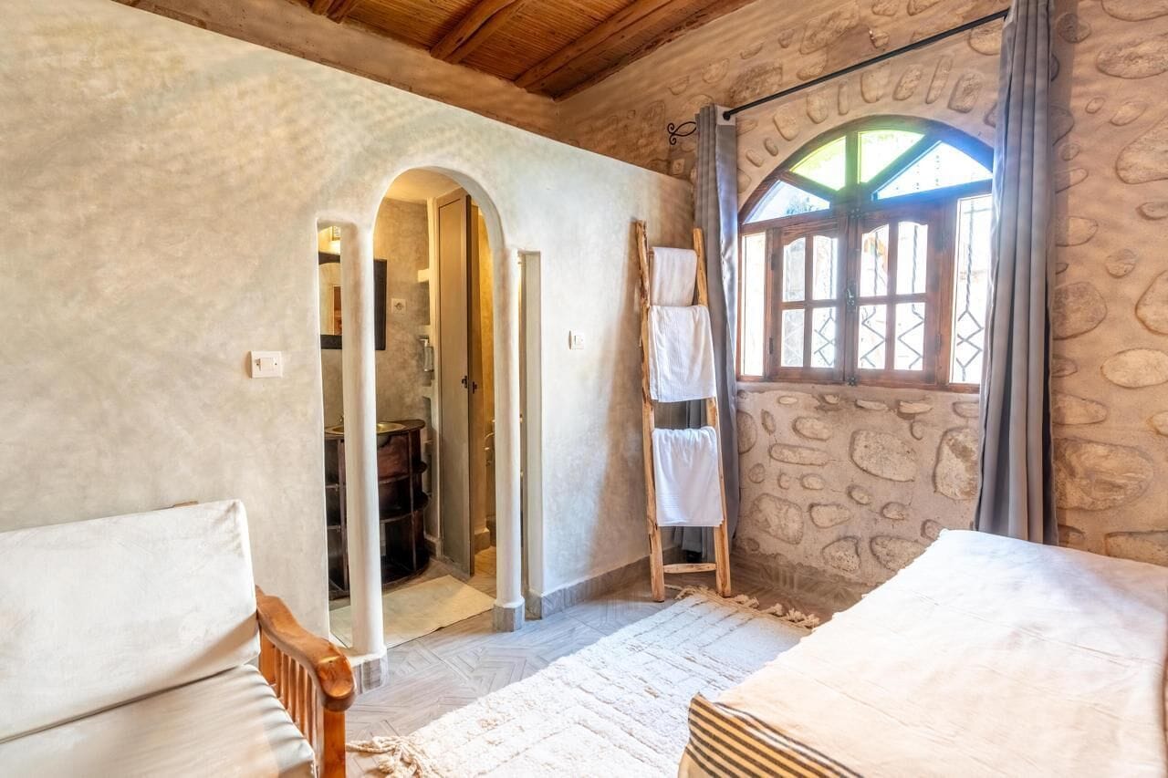A rustic room with a stone wall, wooden furniture, and a window with a view.