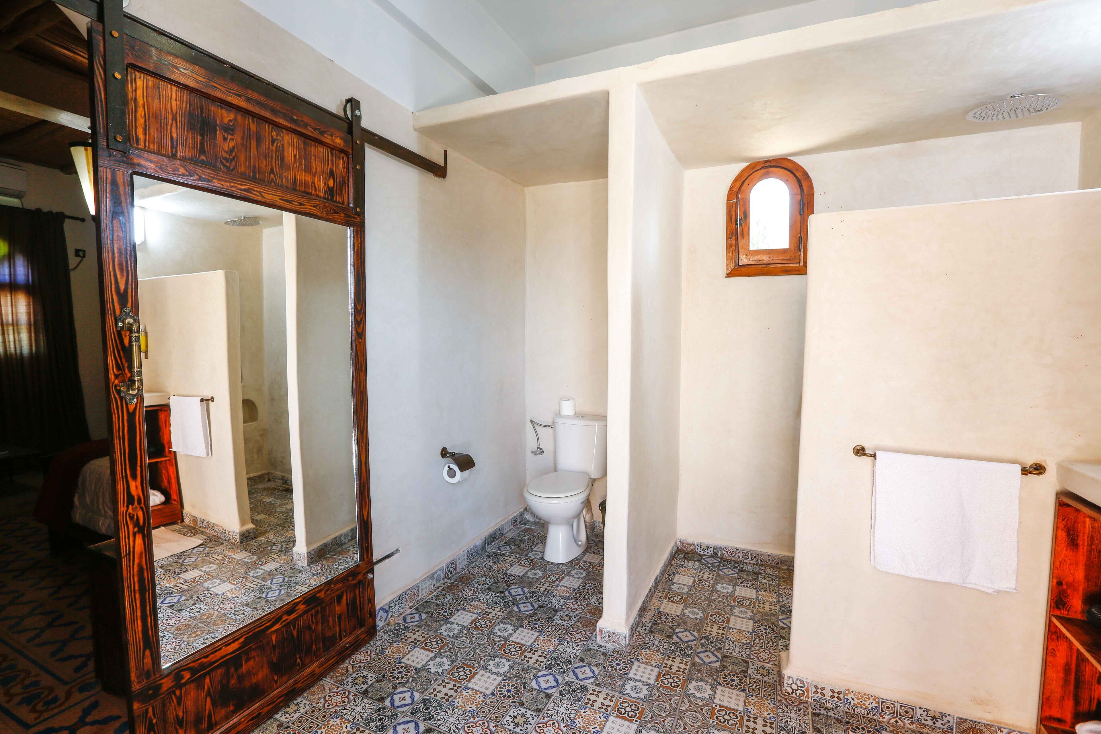 Un bagno con uno specchio con cornice in legno, un WC e un pavimento piastrellato.