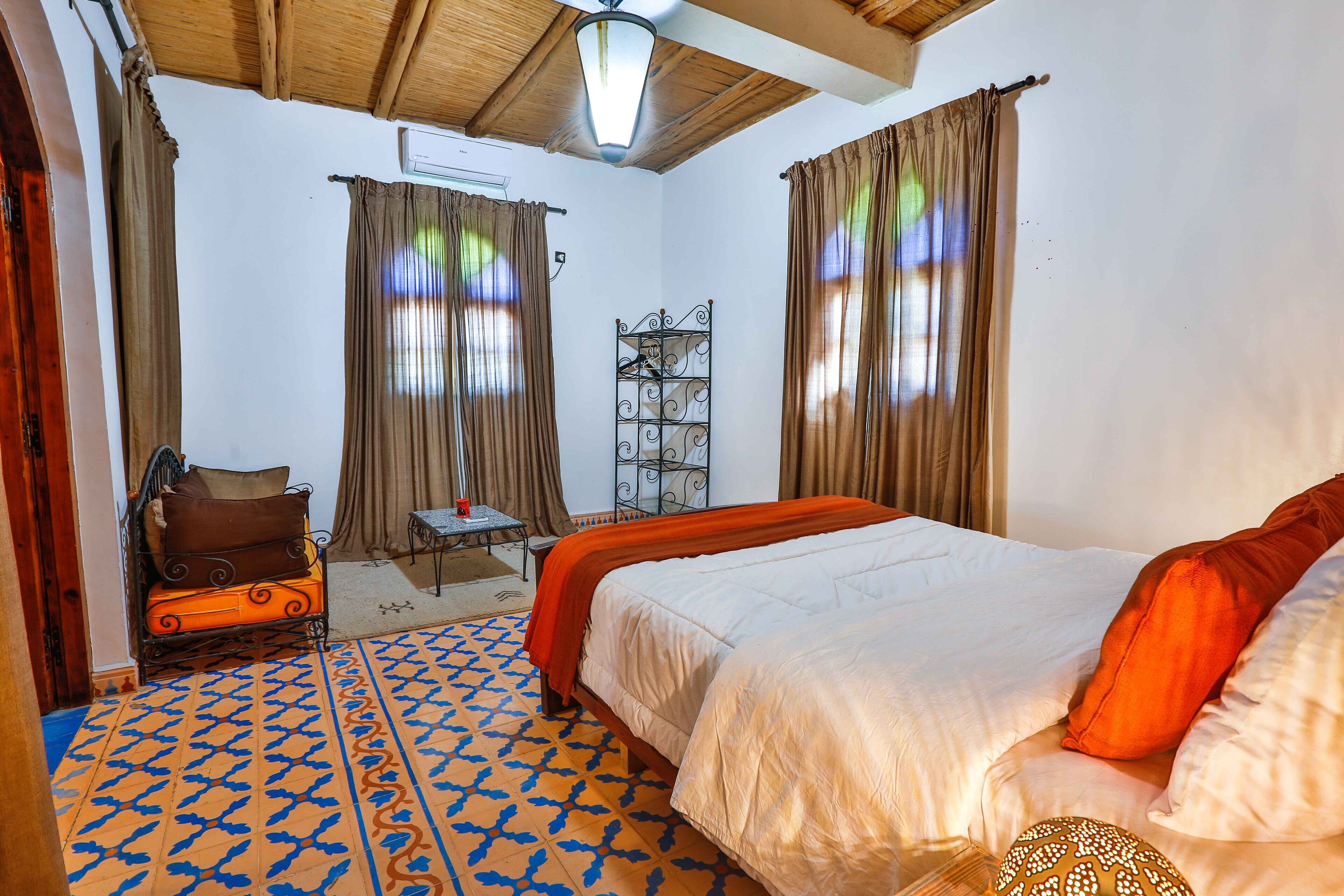 Una habitación de hotel con una cama, una mesita pequeña, una silla y una estantería decorativa de metal.