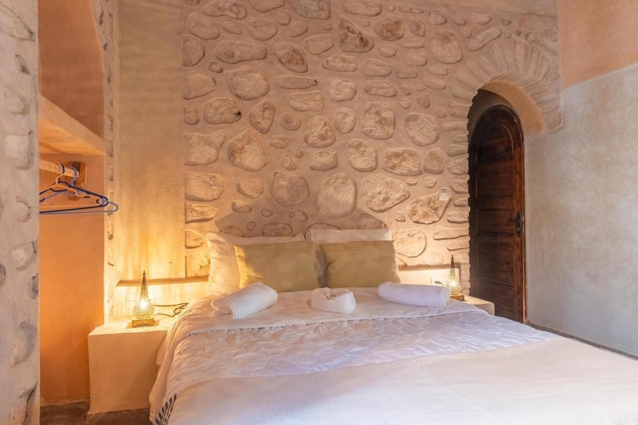 Een slaapkamer met een stenen muur, een houten deur en een bed met witte lakens en handdoeken.