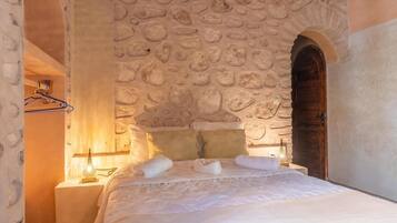 Een slaapkamer met een stenen muur, een houten deur en een bed met witte lakens en handdoeken.