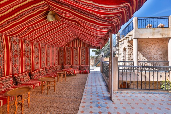 A covered outdoor seating area with patterned rugs and wooden furniture.