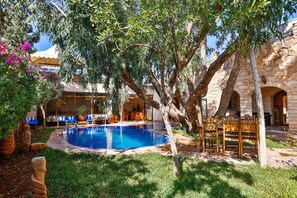 A pool surrounded by lush greenery, stone architecture, and outdoor seating. - Riad Dar Etto (Essaouira)