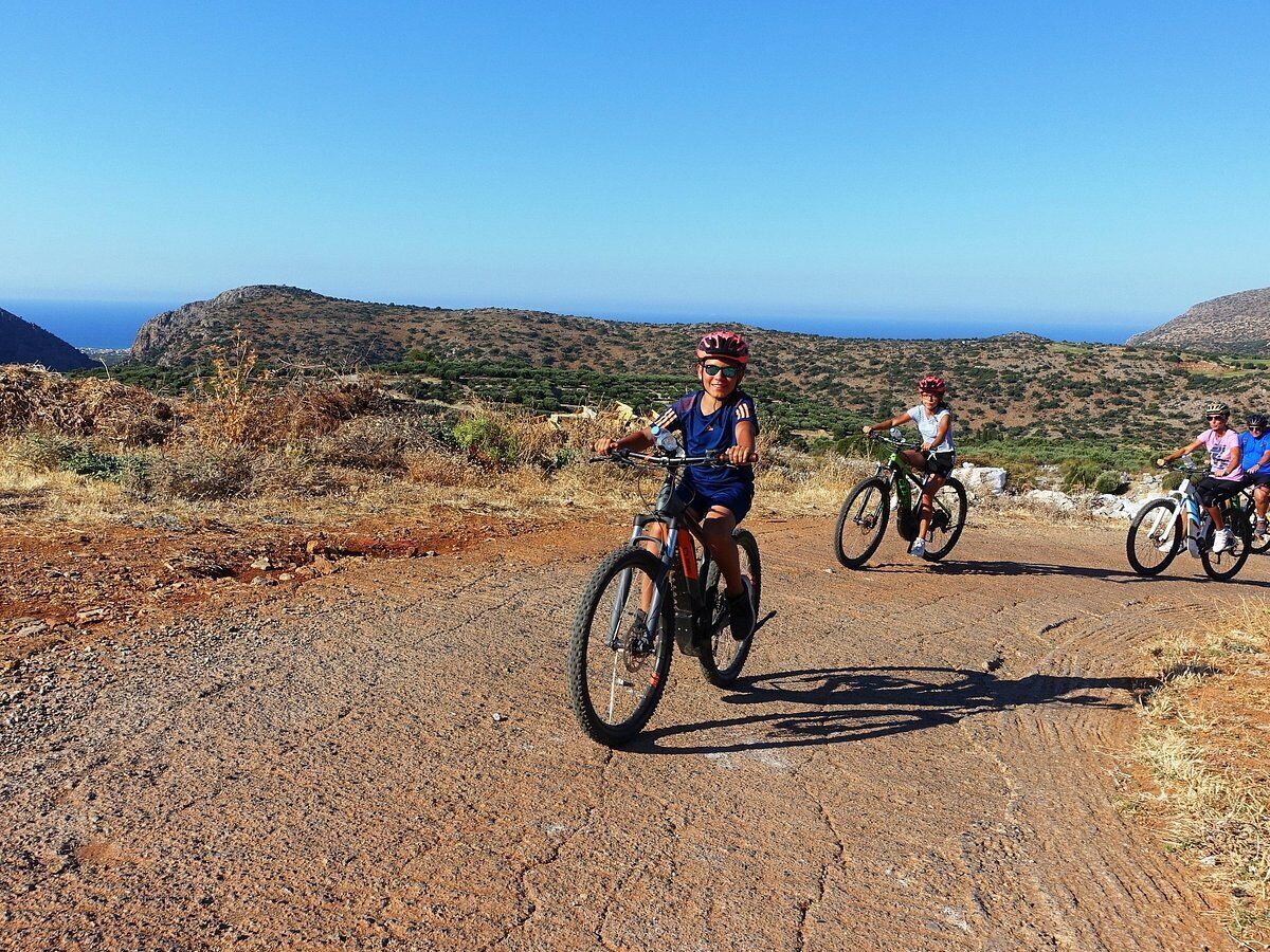 Tres ciclistas en un camino de tierra con un paisaje montañoso al fondo.