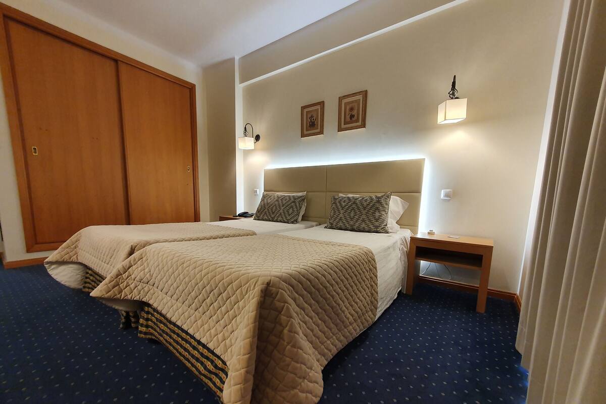 A double bed with a quilted bedspread, two bedside tables, a headboard, and a wardrobe.