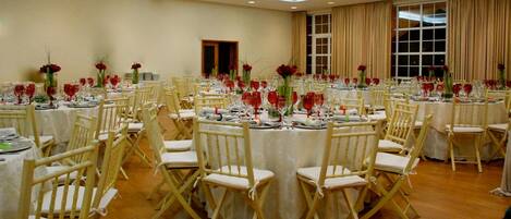 A banquet hall with round tables, white chairs, and red flowers.