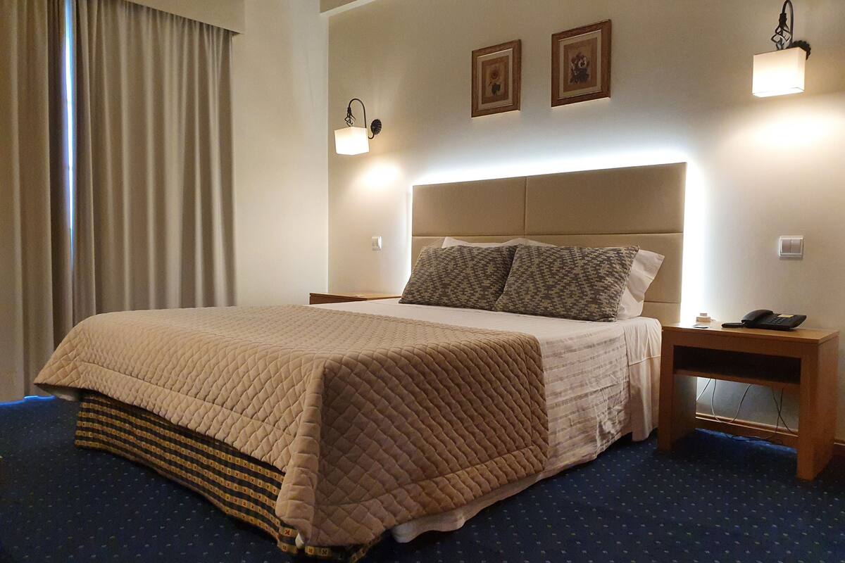 A hotel room with a large bed, a bedside table with a phone, and two wall-mounted light fixtures.