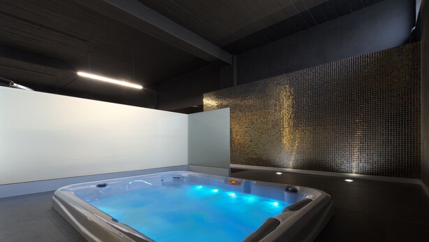 Area benessere moderna con vasca idromassaggio, soffitto scuro e parete rivestita in piastrelle.