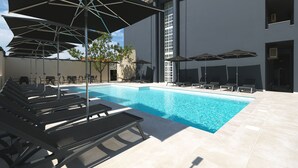 Una piscina con lettini e ombrelloni, circondata da un edificio con pavimento piastrellato e muro in pietra.