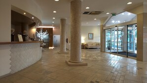 Un'ampia hall con scrivania della reception, imponenti colonne e ingresso con porta in vetro.