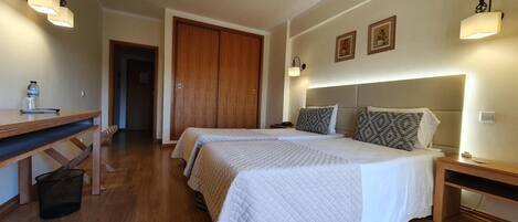 Habitación de hotel con dos camas, suelo de madera, escritorio e iluminación en la pared.