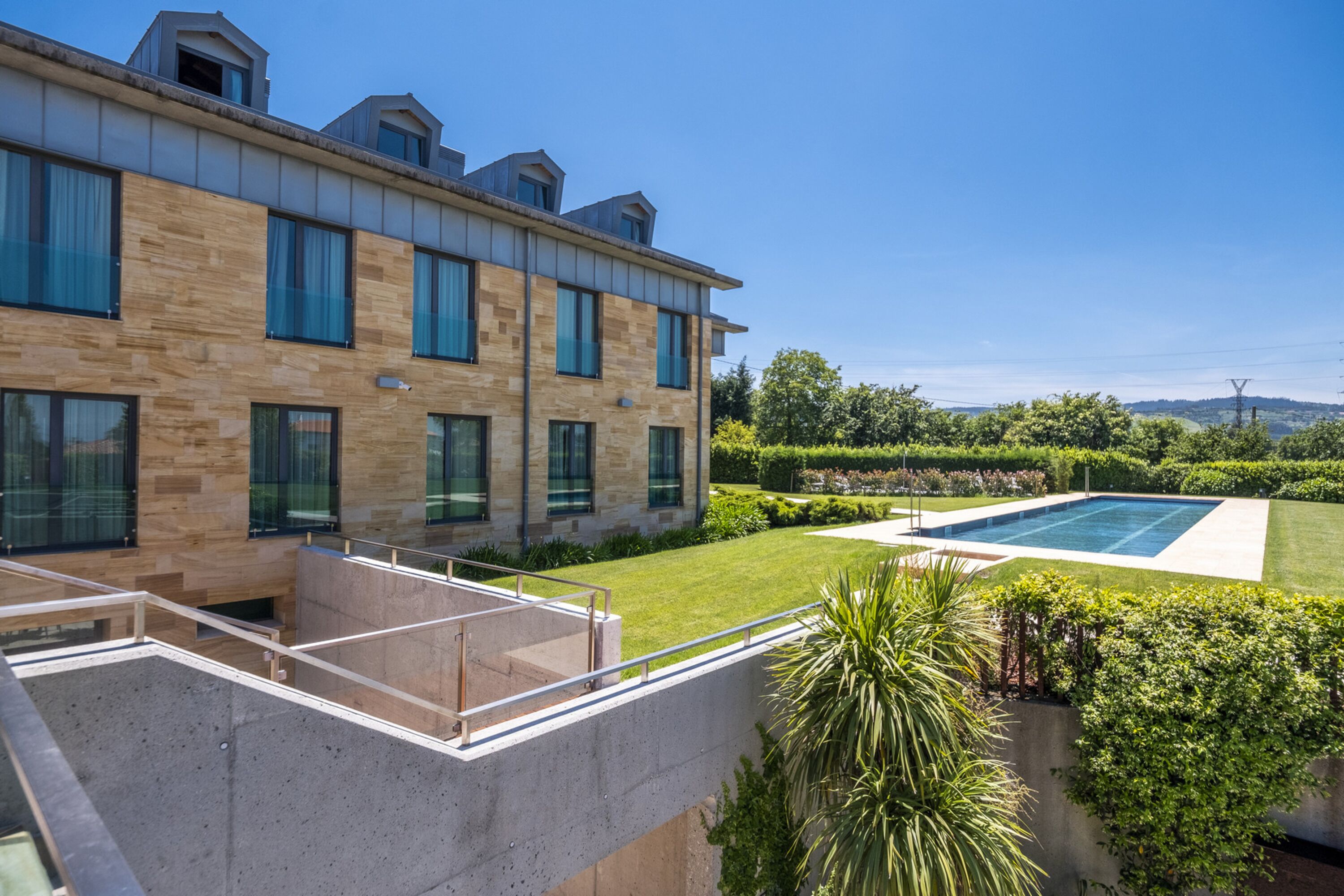 A modern building with a pool, a well-maintained lawn, and a clear sky.
