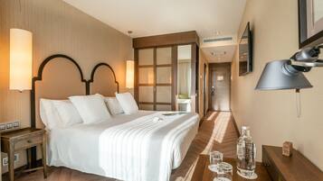 A hotel room with a large bed, bedside lamps, a wooden nightstand, a bedside table with a bottle and glasses, and a mirror on the wall.
