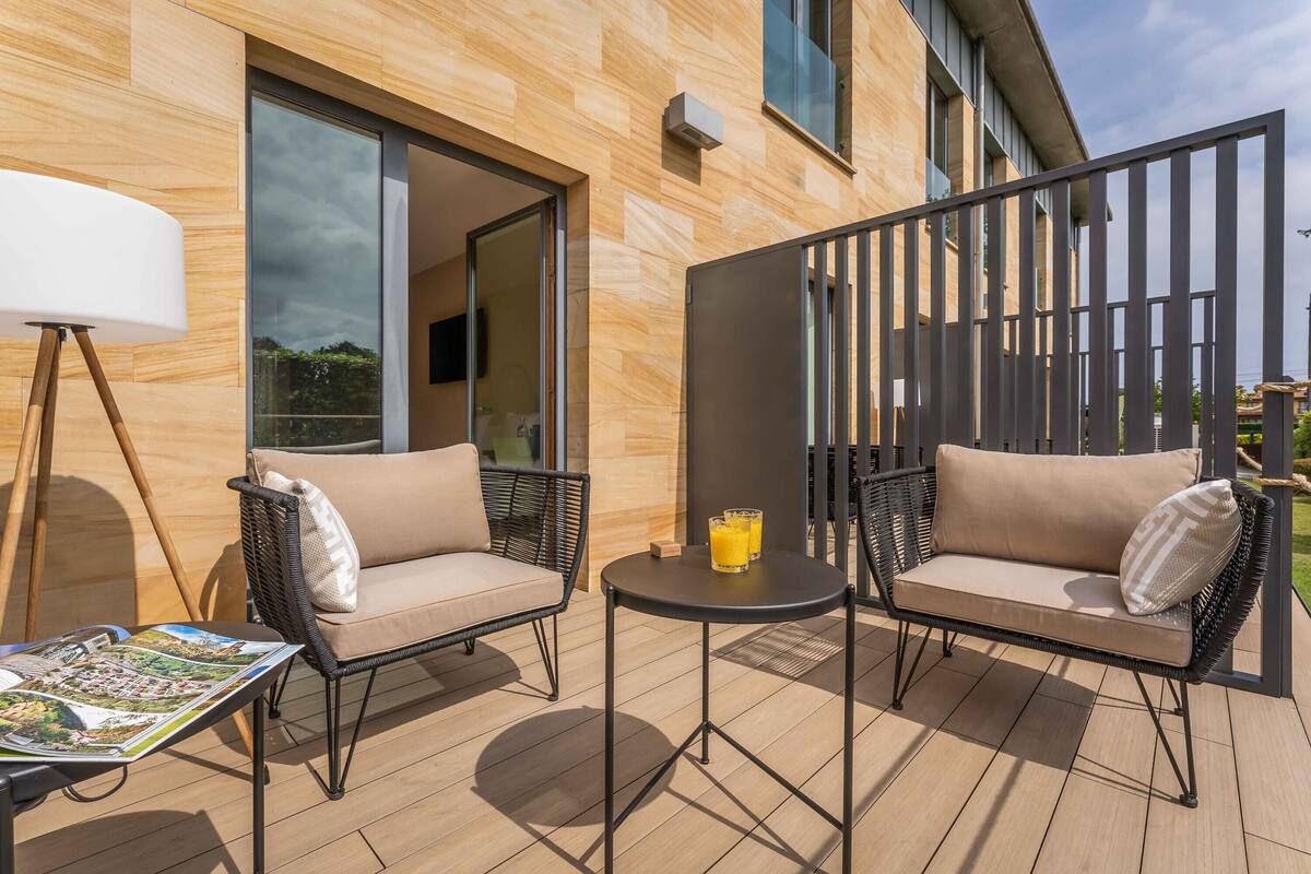 A modern outdoor seating area with two wicker sofas and a small round table, a magazine on the table, and a large window in the background.