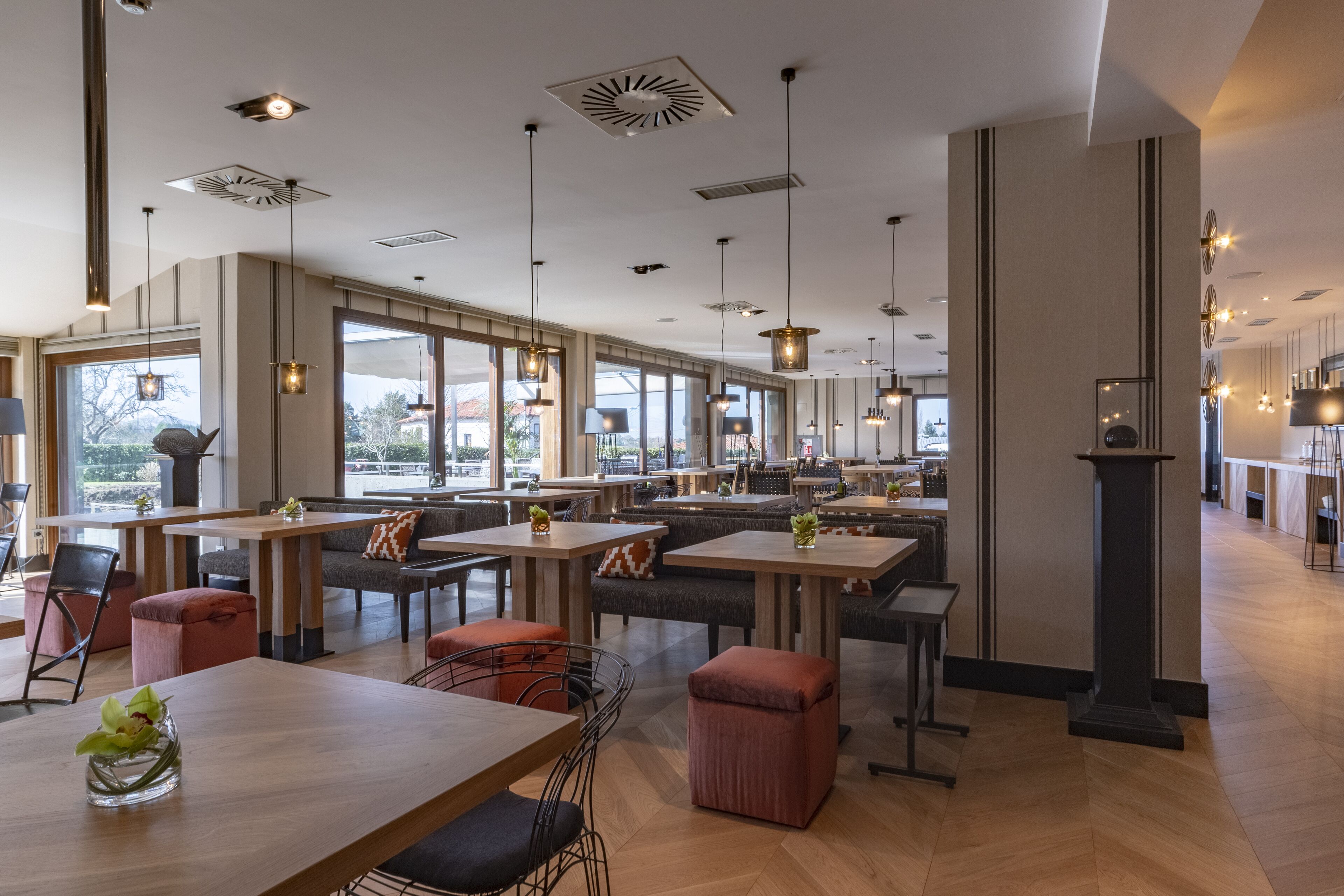Un restaurante espacioso con techos altos, iluminación colgante y amplios ventanales con vistas al exterior.