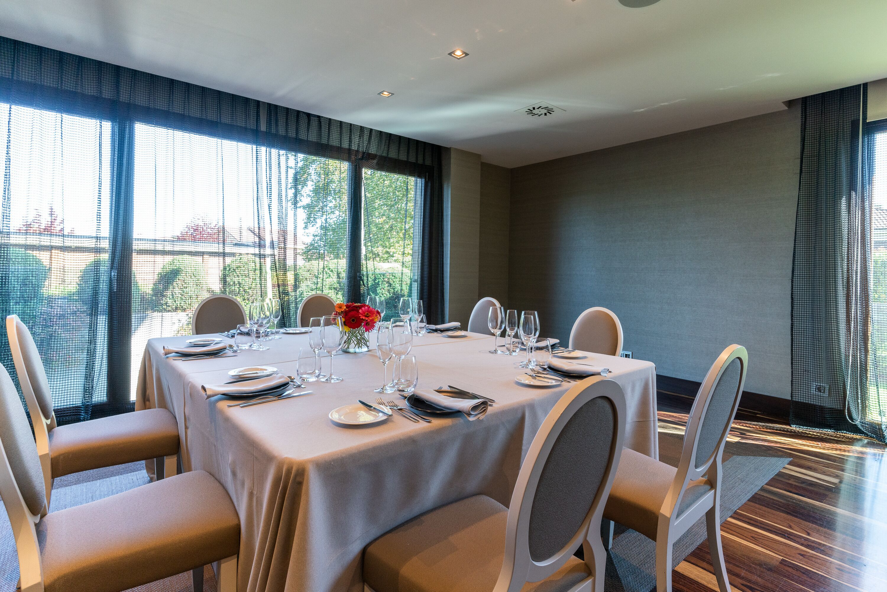 A dining area with a table set for six, large windows, and a view of greenery.