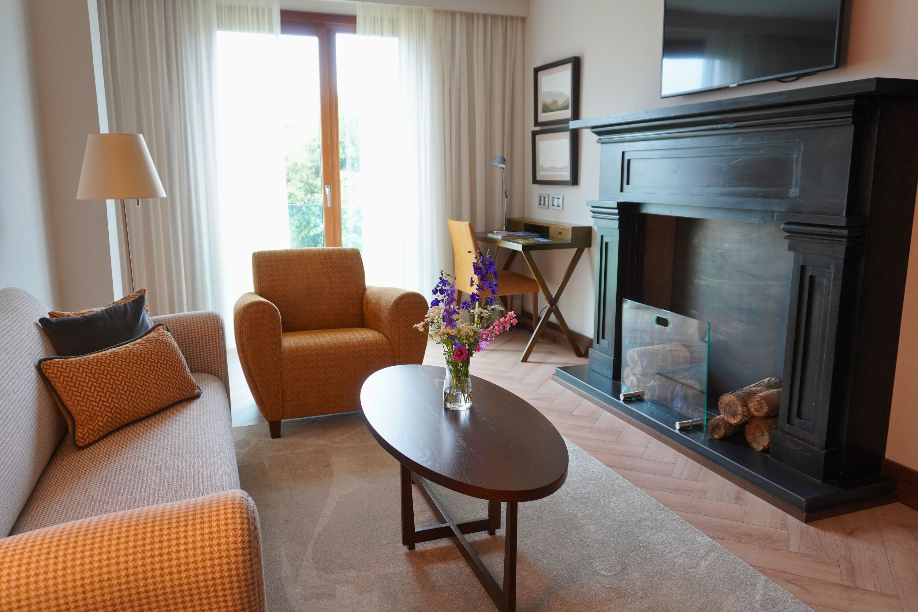 A living room with a sofa, armchair, coffee table, fireplace, and a desk with a lamp.