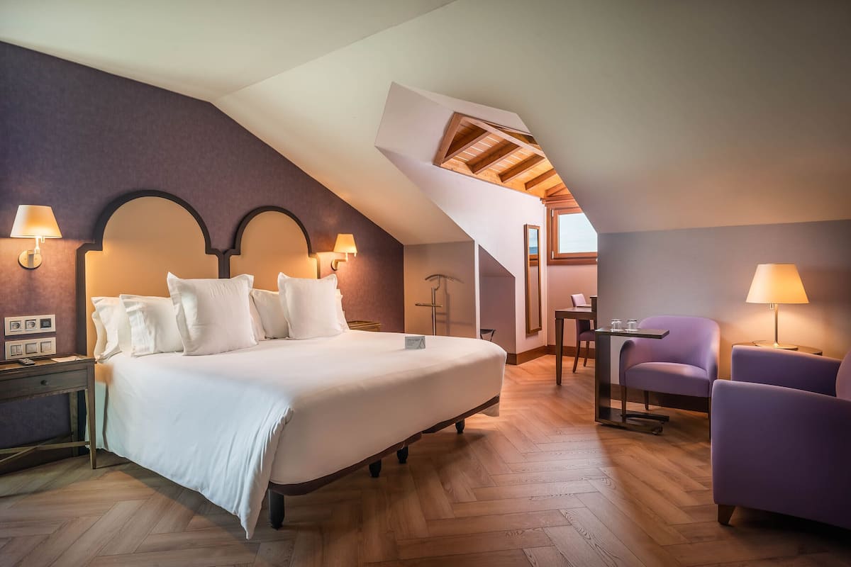 A bedroom with a large bed, two bedside lamps, a chair, and a desk with a lamp.