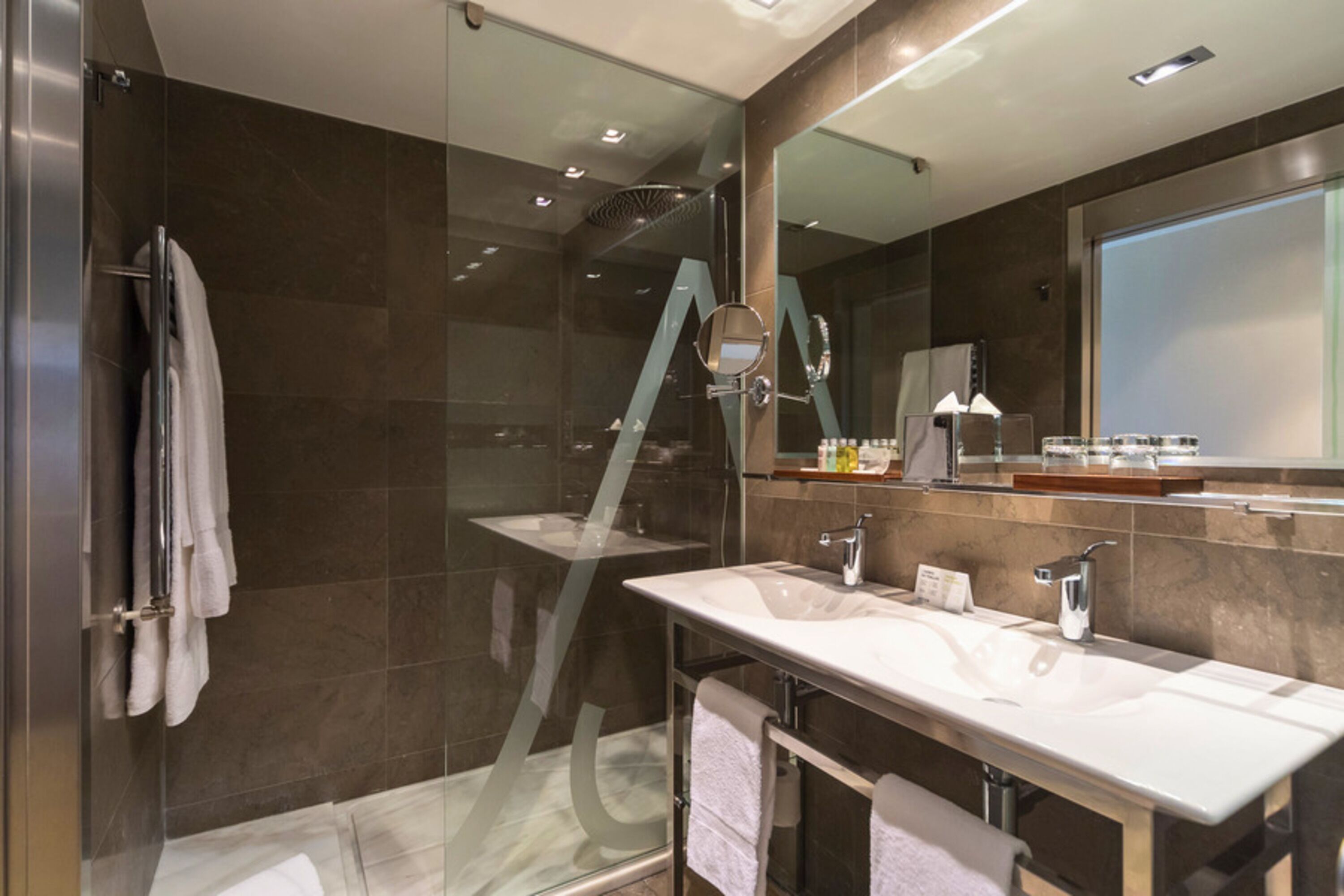 Un baño moderno con ducha de vidrio, un espejo grande y un tocador con lavabo y toallero.