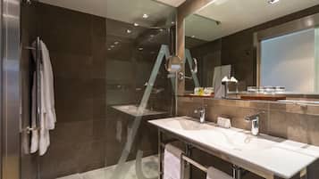 Un baño moderno con ducha de vidrio, un espejo grande y un tocador con lavabo y toallero.