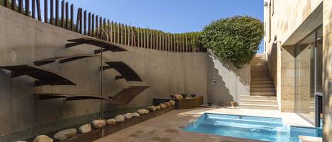 A modern outdoor pool area with a concrete wall, a wooden fence, and a staircase leading to a building.