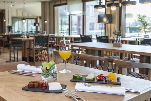 A restaurant setting with wooden tables, chairs, and a glass of orange juice on a table.