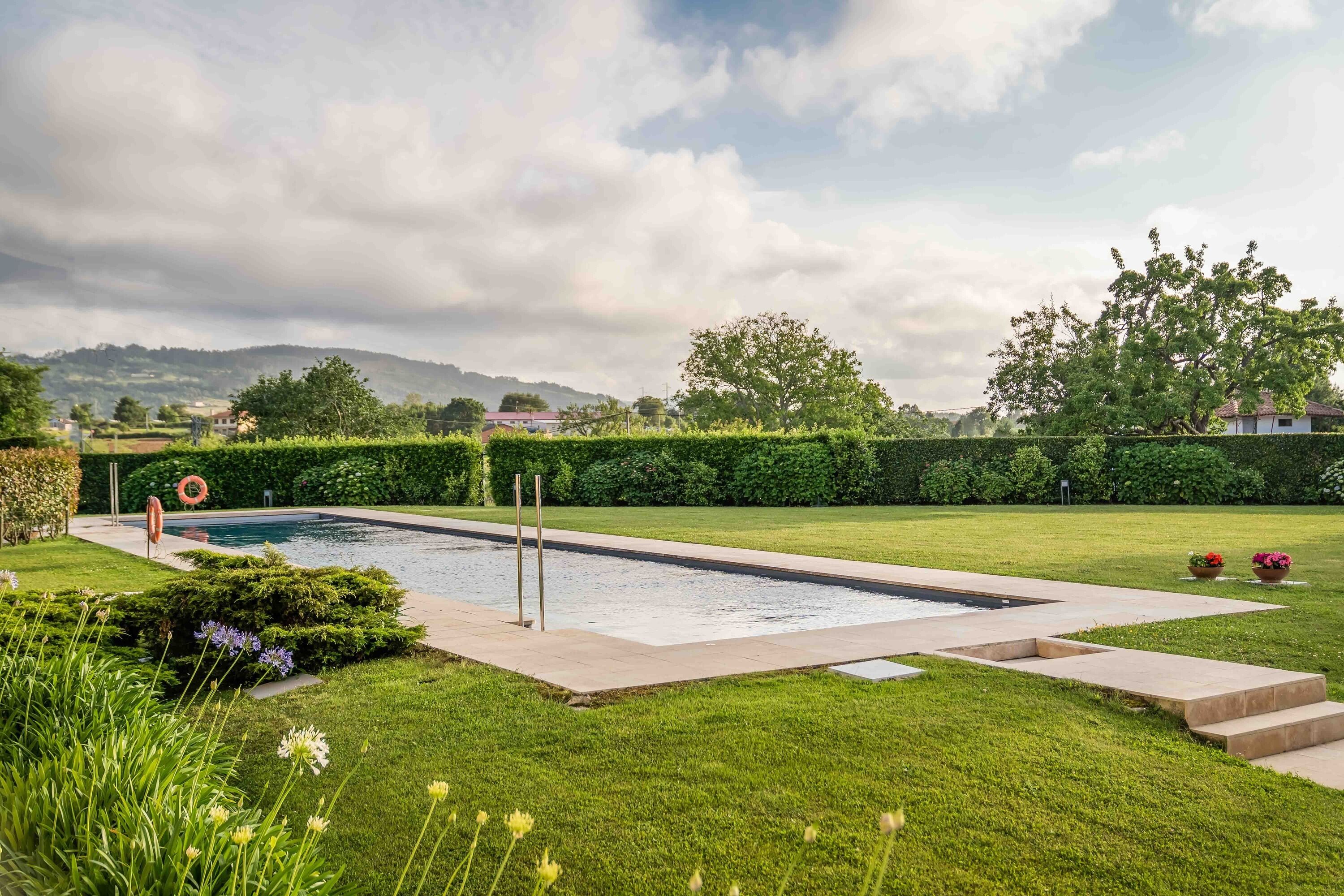 Una piscina rectangular con solárium empedrado, rodeada de césped y setos bien cuidados.