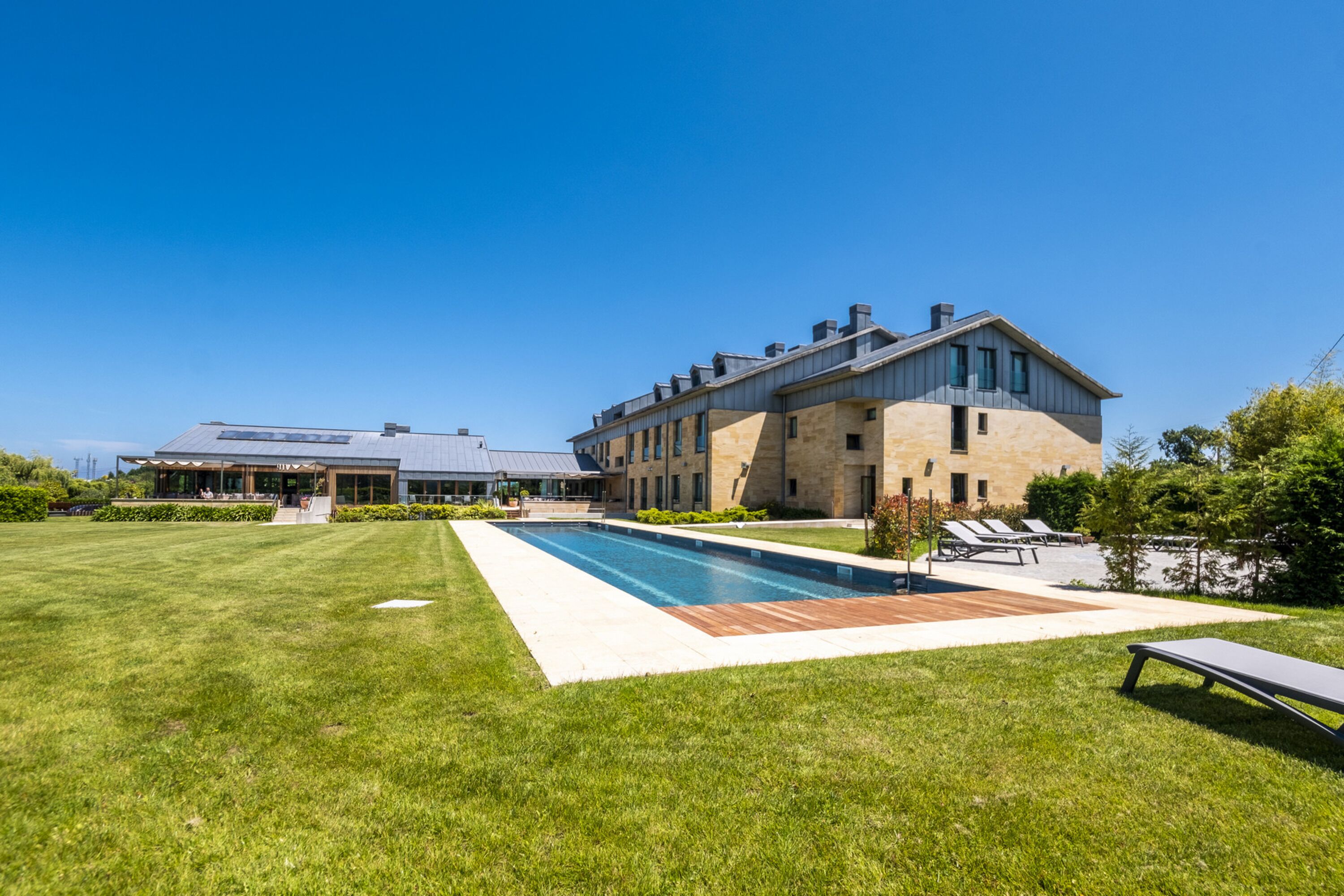 A modern building with a swimming pool, a lawn, and lounge chairs.