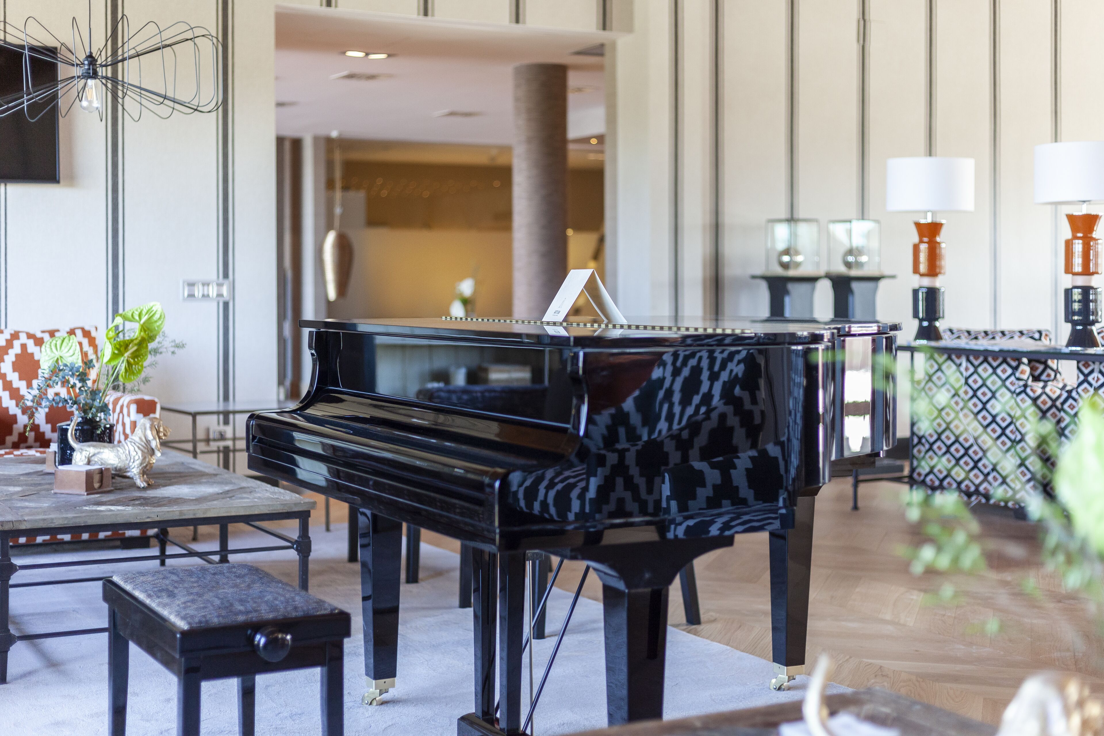 A grand piano in a spacious, elegantly furnished living room with a patterned sofa, a coffee table, and a decorative plant.
