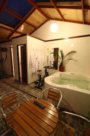A bathroom with a bathtub, a shower, a wooden table with chairs, and a potted plant.