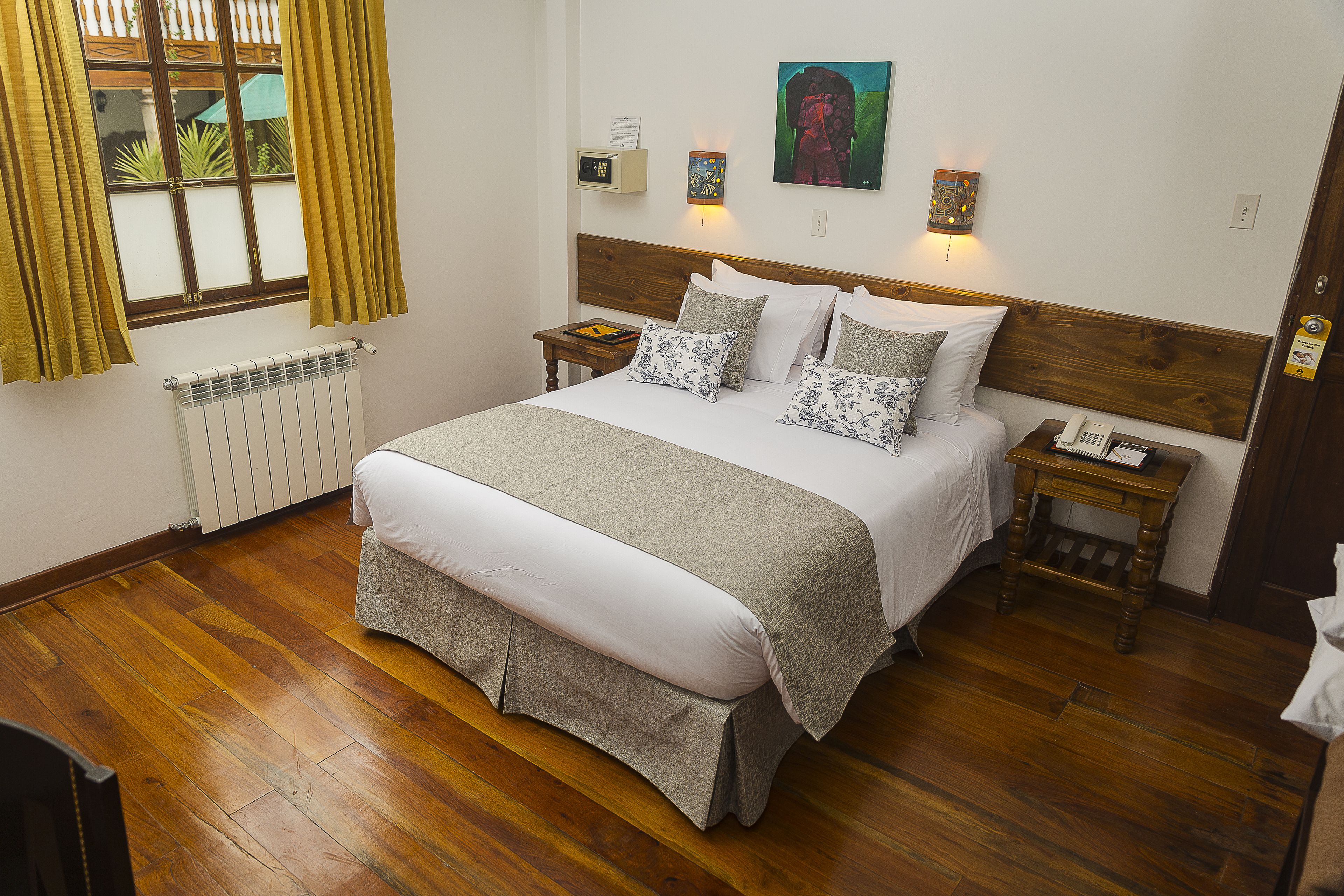 A neatly made bed with a wooden headboard, a bedside table with a lamp, and a window with curtains.