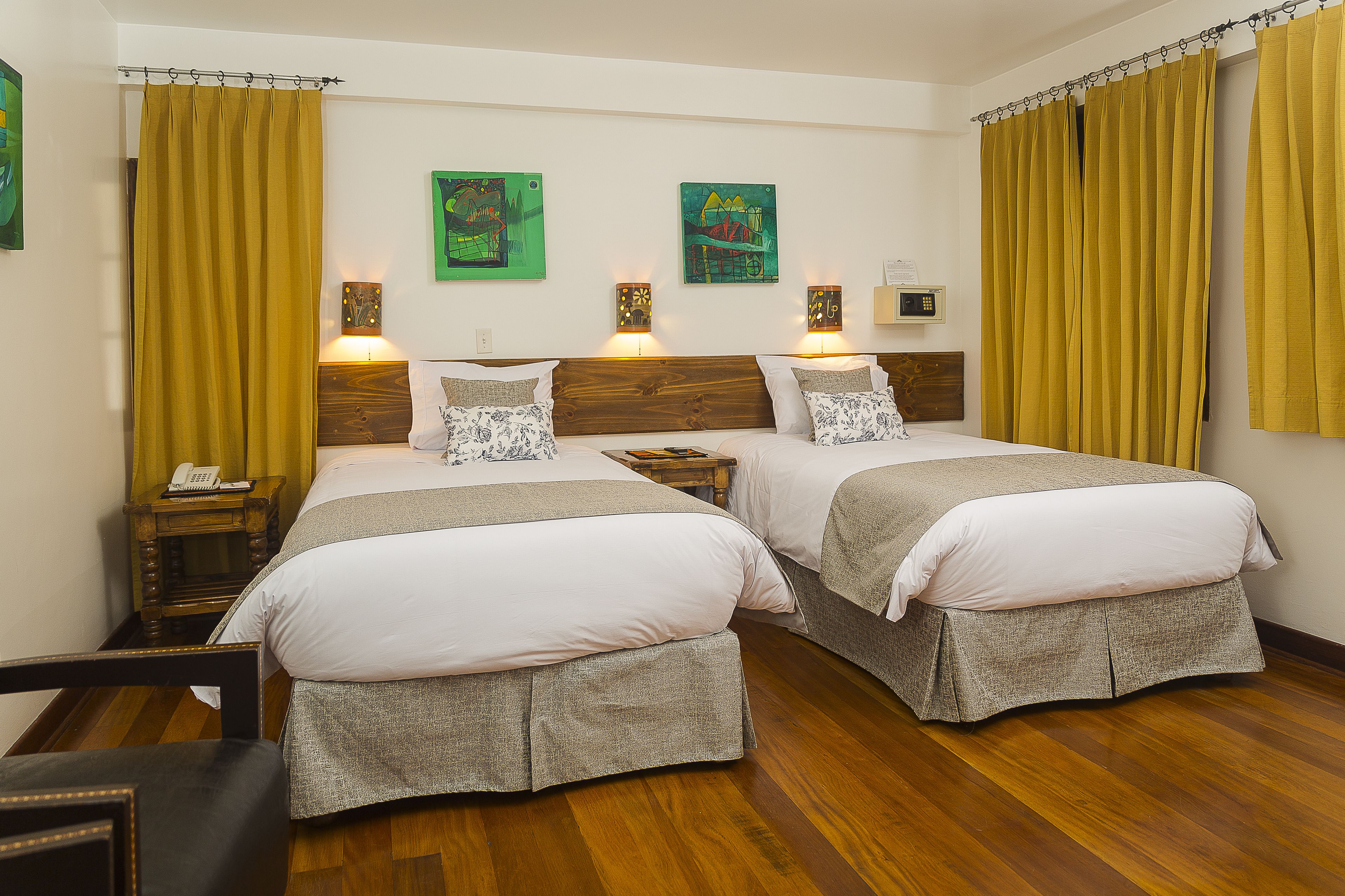 Habitación de hotel con dos camas, suelo de madera y obras de arte en las paredes.