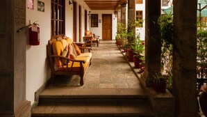A covered corridor with wooden benches and potted plants, leading to a door. - Hotel Rumi Punku (Cusco)