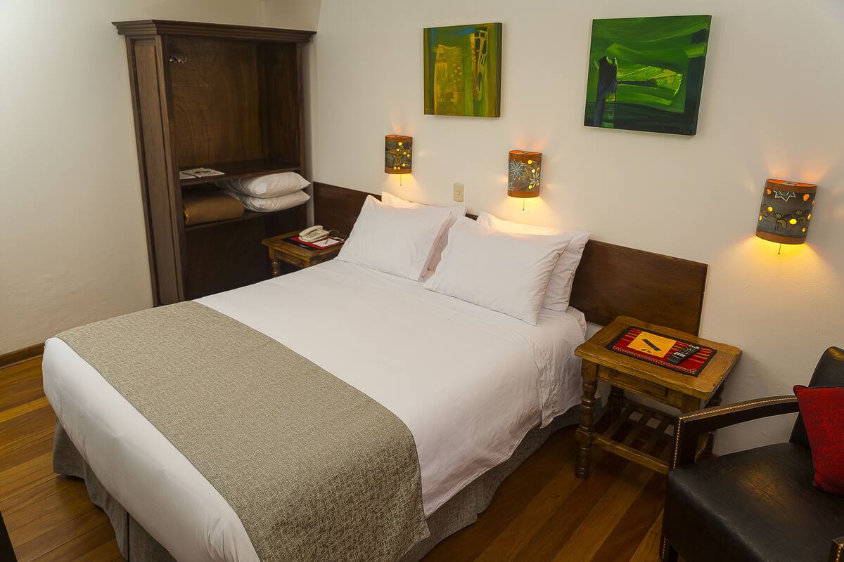A neatly made bed with white linens, a wooden nightstand with a lamp, and a wooden wardrobe.