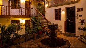 A courtyard with a fountain, a staircase, and a building with a sign. - Hotel Rumi Punku (Cusco)