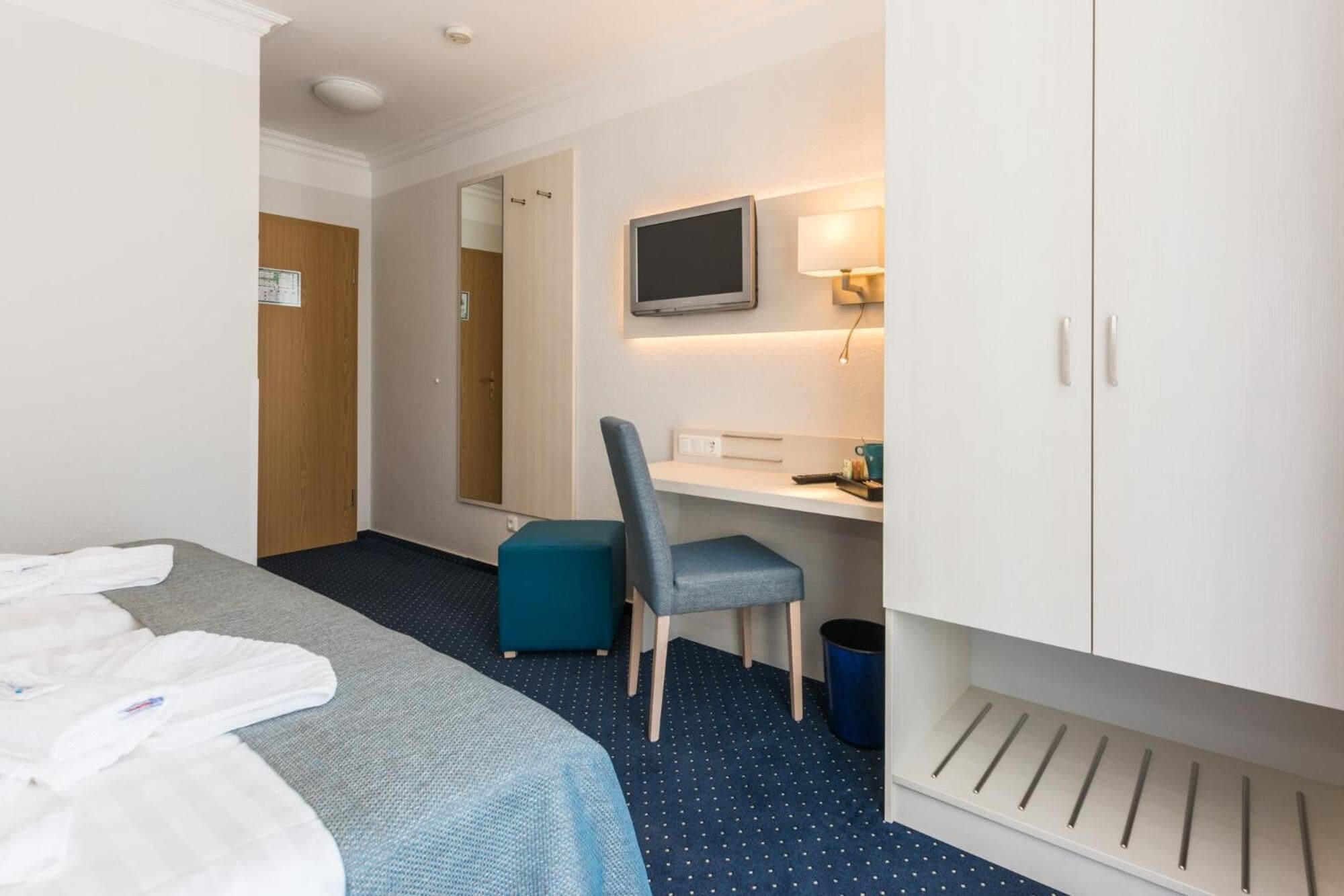 Ein Hotelzimmer mit Bett, Schreibtisch mit Stuhl, Fernseher und Kleiderschrank.