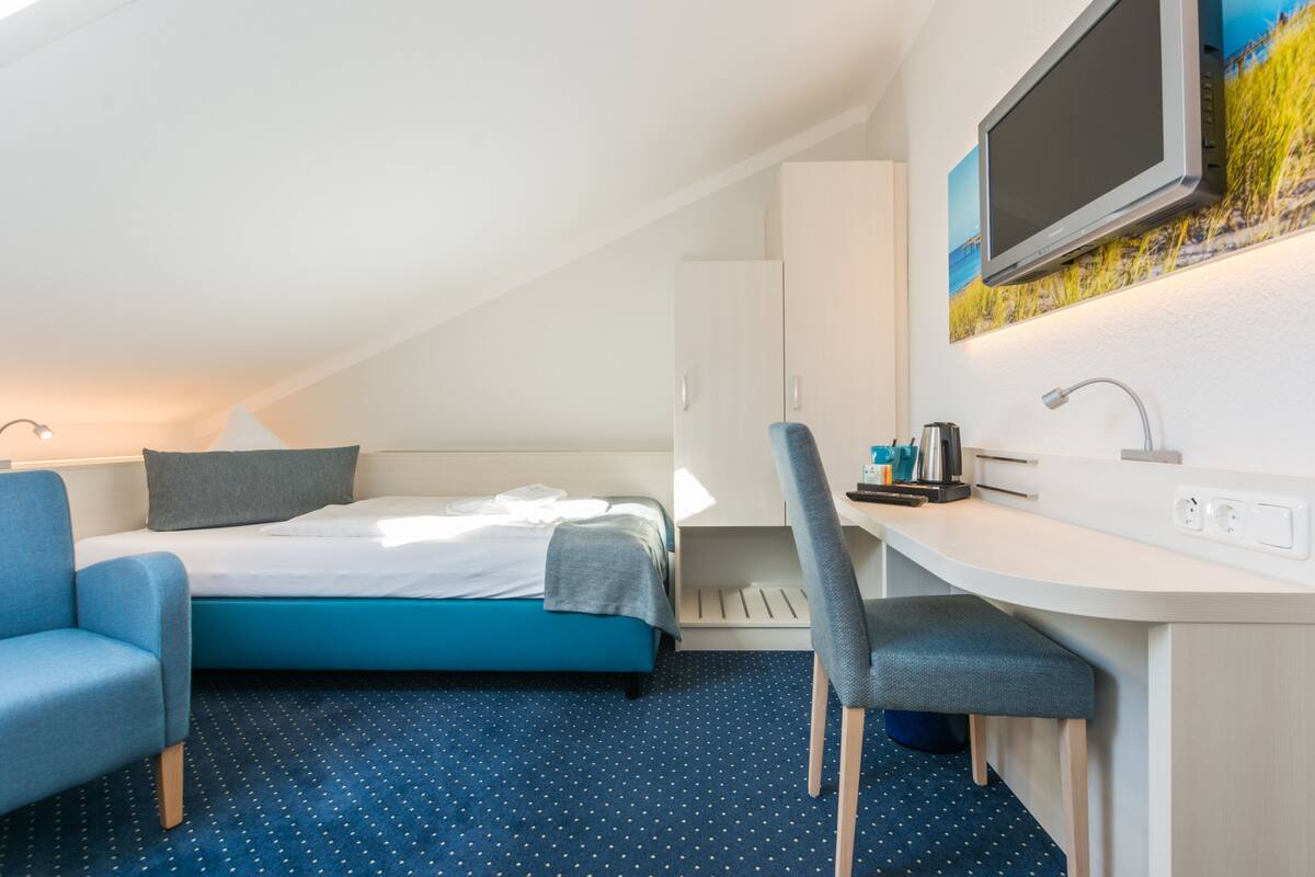 A modern hotel room with a bed, a desk, a chair, and a television.