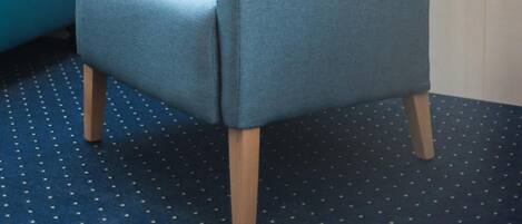 Een kamer met een blauwe fauteuil, een bed met een blauw hoofdeinde, een dakraam en een kleine tafel met een lamp.