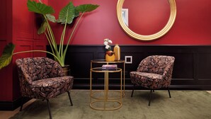 Une pièce comprenant deux fauteuils à motifs, un miroir rond et une petite table sur laquelle se trouvent un vase et des livres.