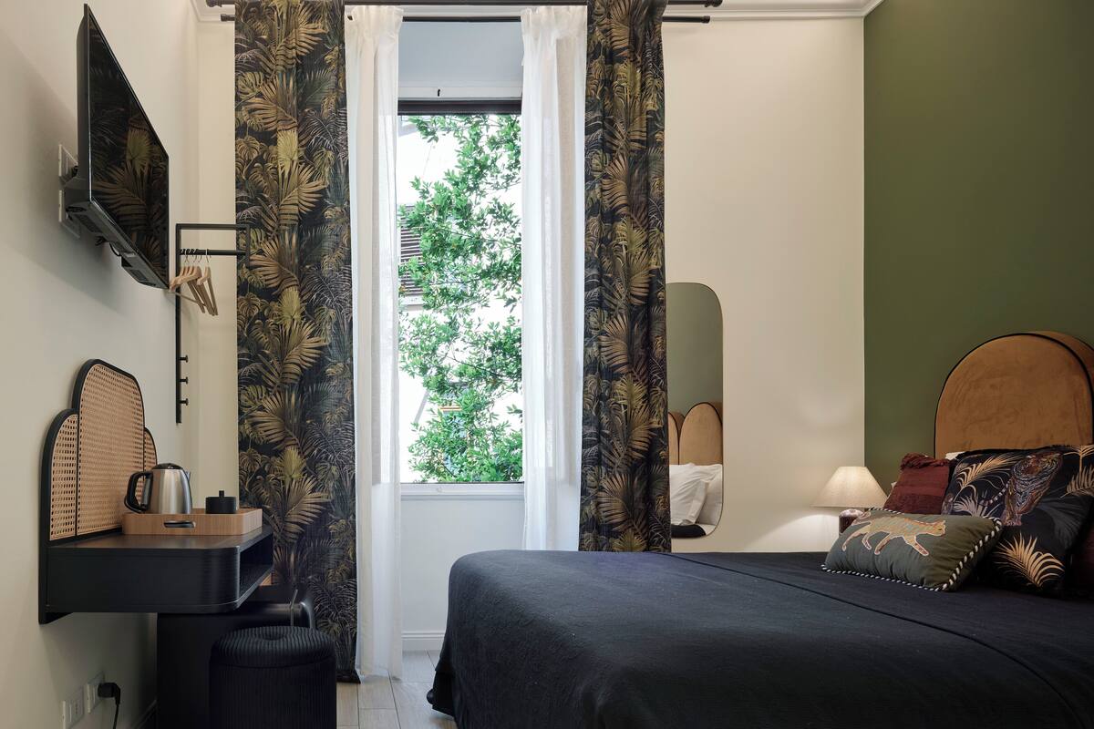 Een slaapkamer met een bed, nachtkastje, lamp en een raam met gordijnen.