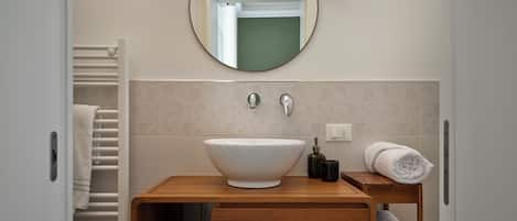 A modern bathroom with a round mirror, a white sink, and a wooden vanity.